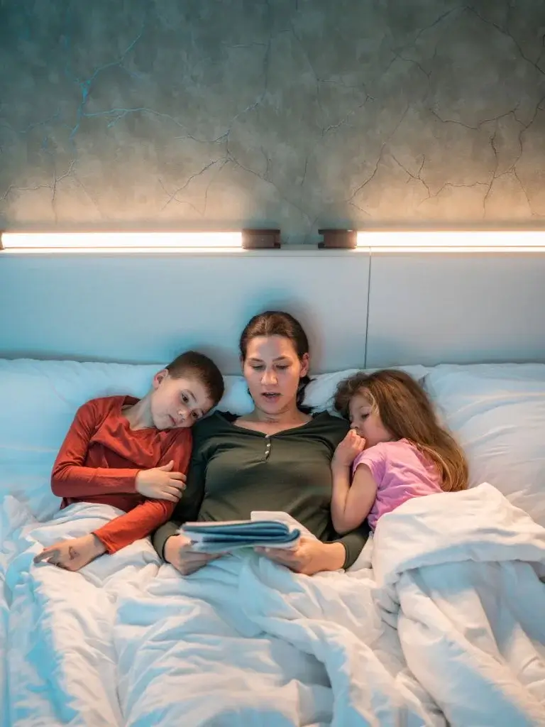 a mom telling bedtime stories to her daughter and son in the bed