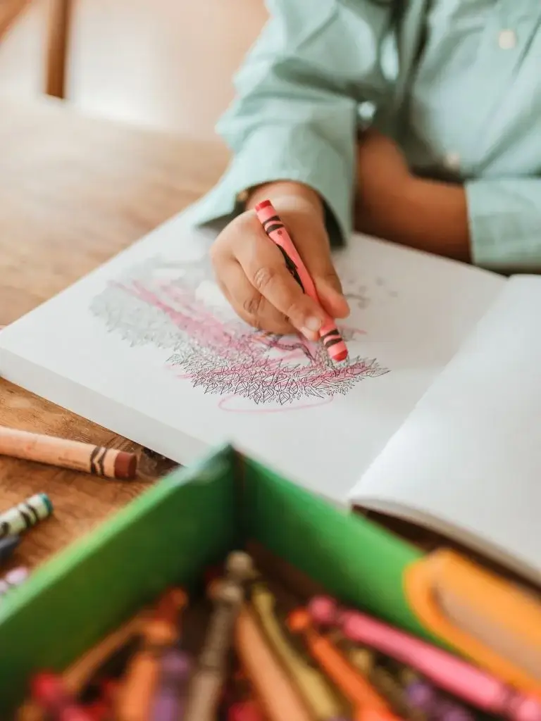 shot of a kids' hand coloring on paper with a crayon 