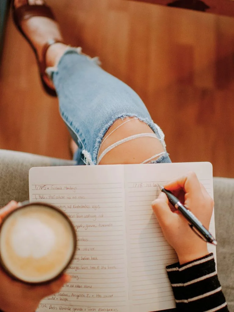 A top shot of a woman writing her journal wit a cup of coffee in hand