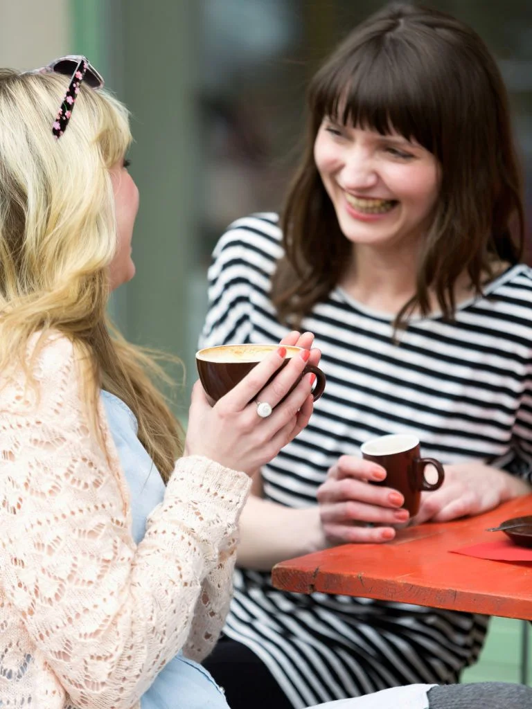 a shot of two women talking to each other with some tea in hand