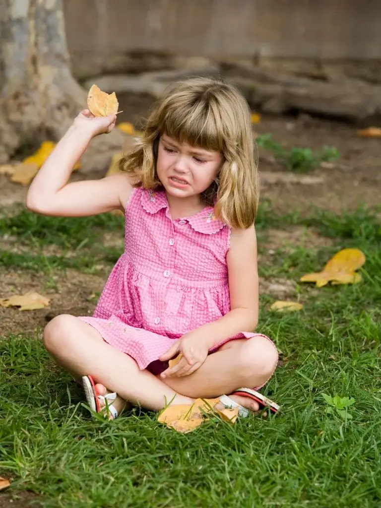 an upset toddler sitting on grass