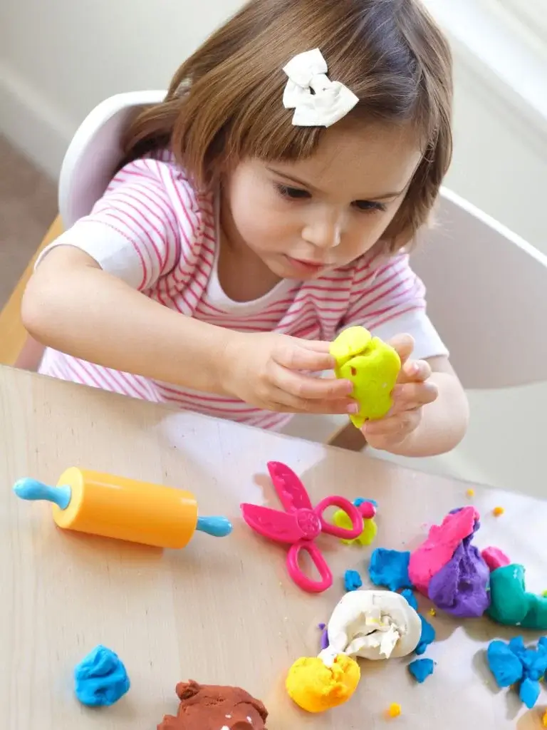 a toddler playing with colorful playdough 