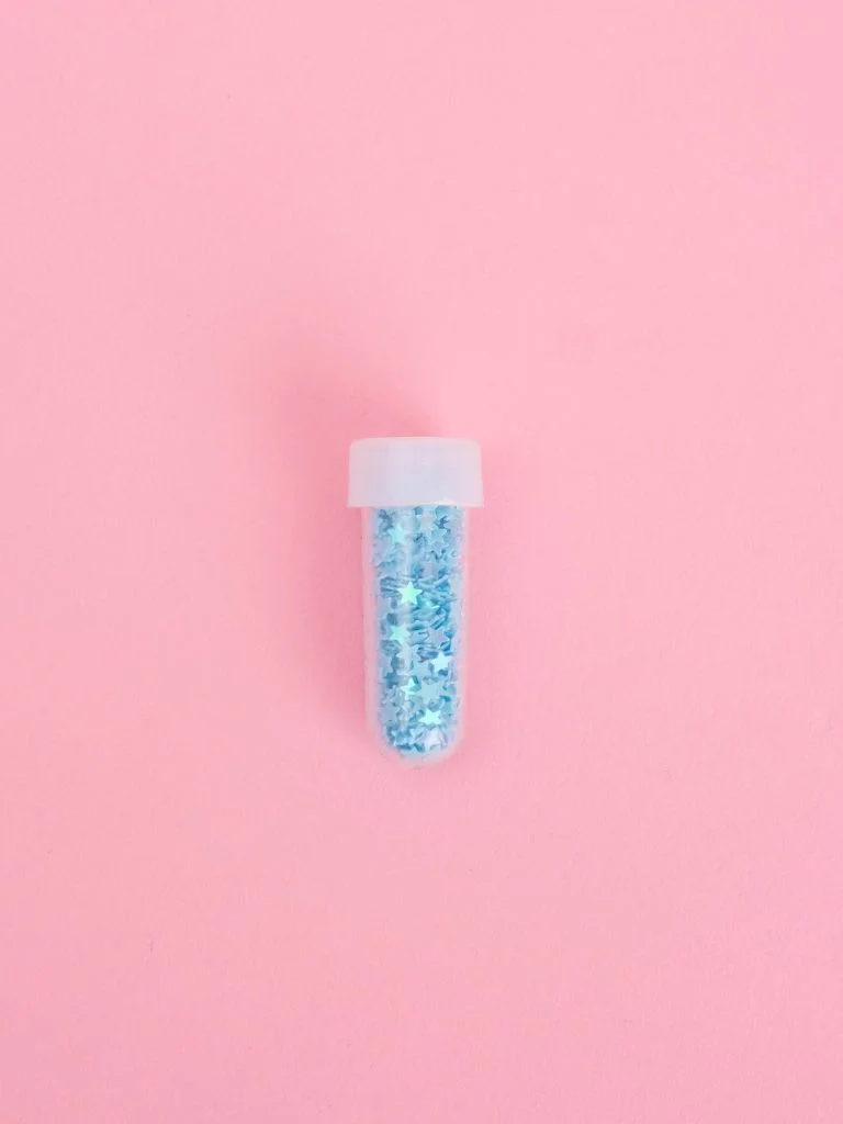 a small glitter bottle behind a pink background
