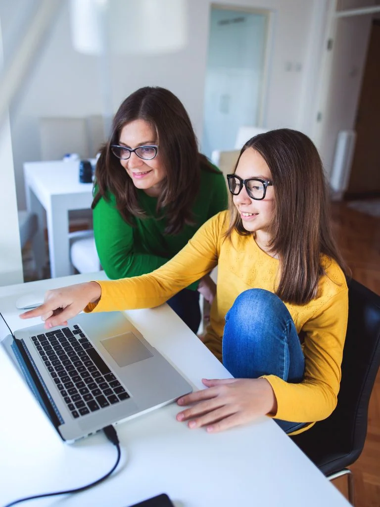 a shot of a mom and her teenager daughter looking at laptop together
