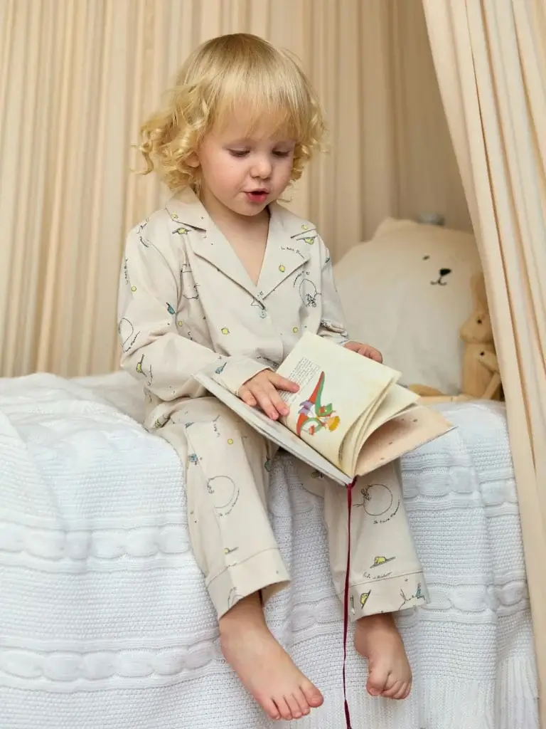 a toddler sitting on a bed with a book in her hand