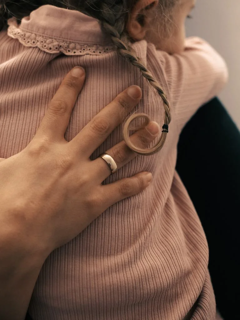 a shot of a mom's hand on the back of her daughter while hugging
